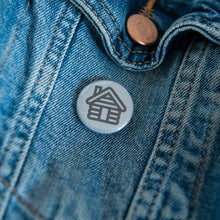 Load image into Gallery viewer, A badge on a jean jacket with a grey background and a house illustration in black.