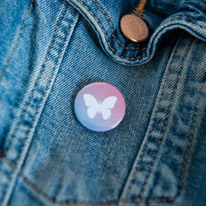 A badge on a jean jacket with a purple and pink background and a butterly illustration in white. 