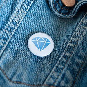 A badge on a jean jacket with a white background and a diamond illustration in blue. 