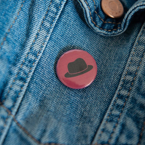 A badge on a jean jacket with a red background and a hat illustration in black. 