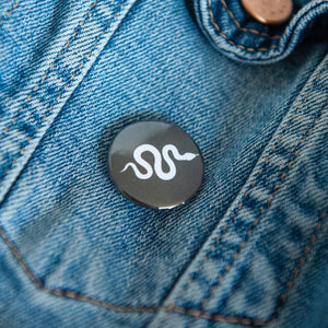 A badge on a jean jacket with a black background and a snake illustration in white. 