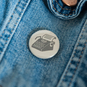 A badge on a jean jacket with a tan background and a typewriter illustration in black. 