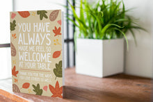 Load image into Gallery viewer, A photo of a card featured on a tabletop next to a white planter filled with a green plant. ​​The card features the words &quot;You have always made me feel so welcome at your table. Thank you for the ways You love others so well&quot; with illustrated leaves surrounding the words. 