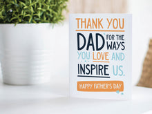 Load image into Gallery viewer, A greeting card is featured on a wood coffee table with a green plant in a white planter in the background. The card features the words  &quot;Thank You Dad for the ways you love and inspire us. Happy Father&#39;s Day.” 
