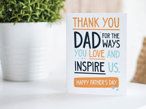 A greeting card is featured on a wood coffee table with a green plant in a white planter in the background. The card features the words  "Thank You Dad for the ways you love and inspire us. Happy Father's Day.” 