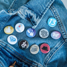 Load image into Gallery viewer, A photo of 10 pin badges on a jean jacket. The badges feature illustrations of a snake, a lighter, a cowboy boot,  cat, a butterfly, a house, a typewriter, a diamond, the number 13, and a black hat. 