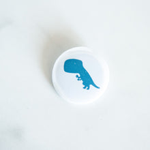 Load image into Gallery viewer, A button pin on a white tabletop. The button features an illustration of a T-Rex. 