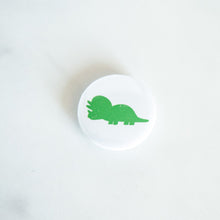 Load image into Gallery viewer, A button pin on a white tabletop. The button features an illustration of a Triceratops. 