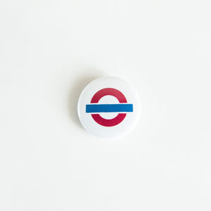 A button on white tabletop. The button features an illustration of a London underground/tube logo. 