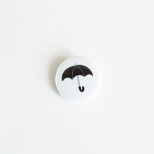 Load image into Gallery viewer, A button on white tabletop. The button features an illustration of a black umbrella. 