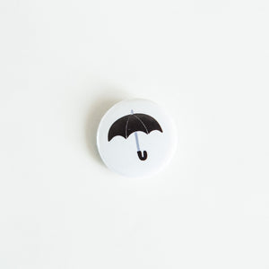 A button on white tabletop. The button features an illustration of a black umbrella. 