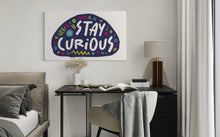 Load image into Gallery viewer, A large flag featured on a bedroom above a desk. The white flag features the words &quot;stay curious&quot; featured inside a a purple shape with sketchy illustrations around. 