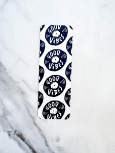 A bookmark on a tabletop. The bookmark features the words "good vibes" inside an illustrated vinyl record.