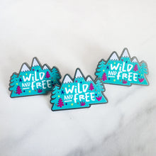 Load image into Gallery viewer, Three enamel pins featuring the words &quot;wild and free&quot; inside illustrated mountains with illustrated trees. 