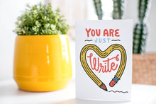 Load image into Gallery viewer, A greeting card is on a table top with a yellow plant pot and a green plant inside. The card features the words “You are just write”with an illustrated pencil in the shape of a heart.