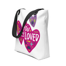 Load image into Gallery viewer, A side view of a white tote bag with black handles on a white background. The bag features a design with the words &#39;you are loved&#39; inside two illustrated pink hearts with a smaller, purple heart above. 