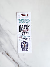 Load image into Gallery viewer, A bookmark laying on a marble tabletop. The bookmark has a white background with the words &quot;Your word is a lamp to my feet and a light to my path&quot; and an illustrated lamp on the bottom. 