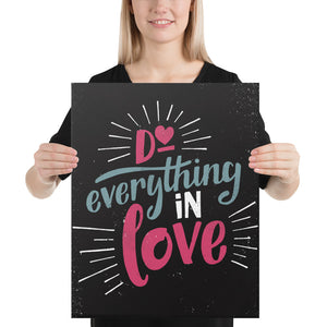 A smiling woman holds up a black art canvas. The canvas reads "Do everything in love" in bright pink and blue hand-lettering style, with white dashes around the words.