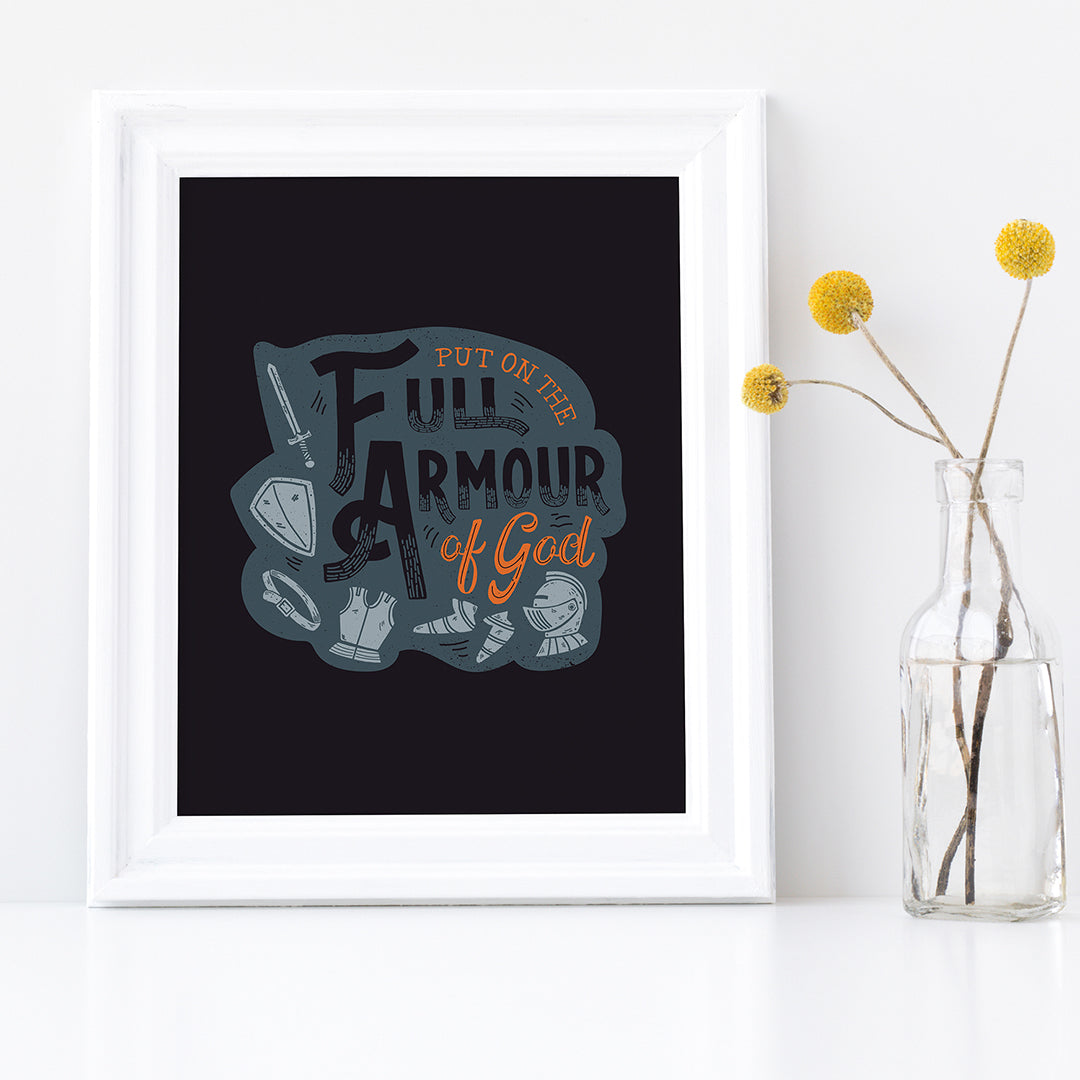 A framed print sits on a white shelf next to a vase of yellow flowers. The print features the quote 'Put on the full armour of God' in black and orange typography, with medieval-style pieces of armour illustrated in pale gray.