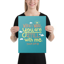 Load image into Gallery viewer, A smiling woman holds up a turquoise art canvas. The canvas reads &#39;When I wake you are still with me, Psalm 139:18&#39; in orange and yellow lettering, illustrated with a small yellow sun and little grey clouds.