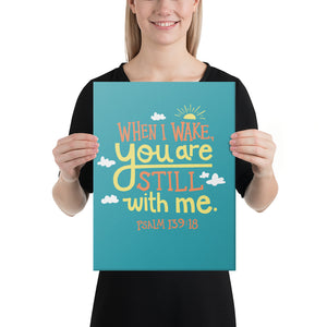 A smiling woman holds up a turquoise art canvas. The canvas reads 'When I wake you are still with me, Psalm 139:18' in orange and yellow lettering, illustrated with a small yellow sun and little grey clouds.