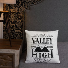 Load image into Gallery viewer, A monochrome square pillow sits on a grey bed with an upholstered headboard. The pillow design is black on a white background, and reads &#39;Every valley shall be lifted high&#39; in a variety of typographic lettering, with flourishes and an illustration of two mountain peaks. Next to the bed is a side table with a lamp.
