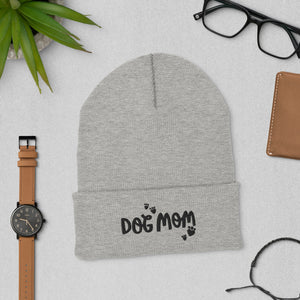 A light grey beanie hat featuring the words Dog Mom in black letters with heart shaped black paws around the words. This is a fun gift for dog moms. 