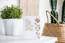 Load image into Gallery viewer, A greeting card is featured on a white tabletop with a white planter in the background with a green plant. There’s a woven basket in the background with a cactus inside. The card features illustrated flowers on the right hand side of the card. The petals are muted pink and the stem and leaves are green and light brown. To the left of the flowers the card reads &quot;I have fallen more in love with you since you became a mother.&quot; 