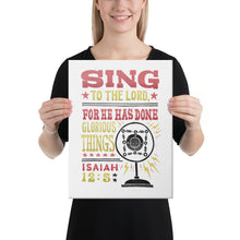 Load image into Gallery viewer, A woman holding a canvas in her hands. The canvas has a white background with the words &quot;Sing to the Lord for he has done glorious things. Isaiah 12:5.&quot; The words are in red, yellow and black. 