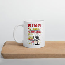 Load image into Gallery viewer, A white mug sitting on a piece of wood. The white mug features hand drawn lettering with the words &quot;Sing to the Lord for he has done glorious things. Isaiah 12:5.&quot; The words are in red, yellow and black.