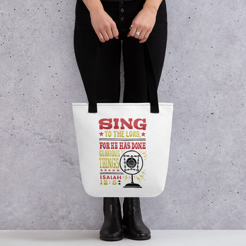 Someone holding a tote bag with black handles and a white fabric bag. The artwork features lettering red, yellow and black reading hand drawn lettering with the words 