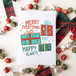 A Christmas card featured on top of some red and white Christmas decorations. The card has a white background with the words "Merry Everything and Happy Always." There are three illustrated Christmas gifts in light red, green and blue with patterns on them.