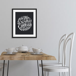 Artwork featured on a wall in a black frame above a kitchen table with a tea set on the table. The artwork is on a black background with some white texture to give a vintage look. The text is in white and reads “Live a life worthy of the calling you have received.” 