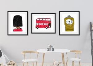 Frames with London illustrations with a white kids' table with kids' block on the table and toys on the ground. Three black frames with London illustrations in the frame. The first illustration is a queen's guard, the second a red double decker bus and the third, an illustration of Big Ben.
