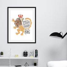 Load image into Gallery viewer, A black frame with illustrated artwork of a lion with lettering reading &quot;Course He Isn&#39;t Safe, But He&#39;s Good. He&#39;s the King.&quot;. The frame is on the wall above a shelf. 