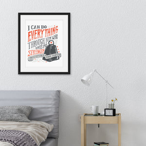 Artwork featured in a black frame in a bedroom above a bed. The artwork is printed on white paper and features black and red hand drawn lettering with the Bible verse Philippians 4:13 "I can do everything through him who gives me strength." 