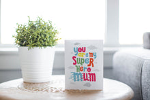 Load image into Gallery viewer, A greeting card is featured on a wood coffee table with a green plant in a white planter in the background. The card features the words “You are my super hero mum” with clouds in the background. 
