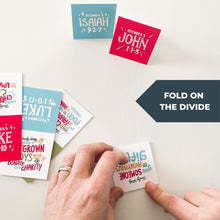 Load image into Gallery viewer, A photo of the cards and hands folding one of the cards with the words &quot;fold on the divide.&quot;