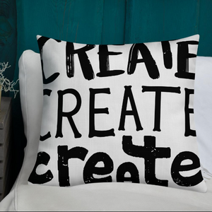 A pillow on a bed with the phrase “create, create, create" in black lettering. The pillow is white.