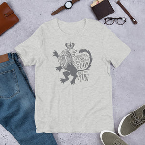A light heather grey short sleeved T-shirt laying flat with objects around it. The T-Shirt features hand drawn illustration of the Chronicles of Narnia lion character Aslan. Inside the illustration there is the quote "Course He Isn't Safe, But He's Good. He's the King."