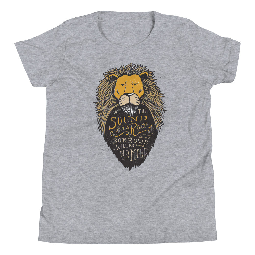 A light grey T-Shirt lays on a white background. The T-Shirt features hand drawn illustration of the Chronicles of Narnia lion character Aslan. Inside the illustration there is the quote “At The Sound of Your Roar, Sorrows Will Be No More.”