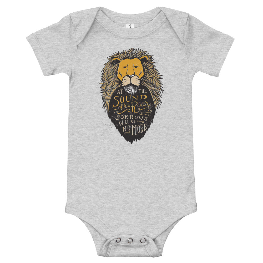 A light grey baby onesie on a white background. The onesie features an illustration of the Aslan character. Inside the illustration there is the quote “At The Sound of Your Roar, Sorrows Will Be No More.”