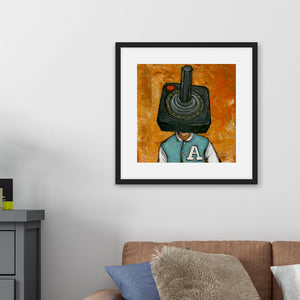 A black frame above a brown sofa with a side table. The artwork in the frame is an illustration of an Atari controller featured as someone's "head."