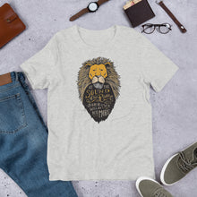Load image into Gallery viewer, A light heather grey short sleeved T-shirt laying flat with objects around it. The T-Shirt features hand drawn illustration of the Chronicles of Narnia lion character Aslan. Inside the illustration there is the quote “At The Sound of Your Roar, Sorrows Will Be No More.”