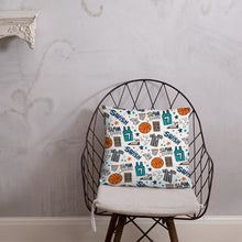 Load image into Gallery viewer, A pillow on a chair against a grey wall. The pillow is white features hand drawn illustrations of basketball themed items.