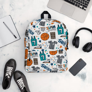 A backpack is placed on a table with a laptop, notebook, shoes, headphones and a mobile phone. The backpack has a white background with a basketball themed pattern backpack featuring illustrated basketballs, basketball jerseys, whistles, referee shirts, basketball hoops, stars, basketball shoes, fun play sketches and the word "swish." The backpack straps are black. 
