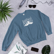 Load image into Gallery viewer, A indigo blue sweatshirt laying with jeans and shoes. The navy hoodie includes the phrase “Be Adventurous” in white with arrows pointing to the word “be” and a mountain illustration underneath the word “adventure.”
