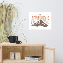 Load image into Gallery viewer, A canvas on the wall above a shelving unit. The artwork on the canvas has the words “Be adventurous” with arrows pointing to the word “be” and a brown mountain illustration underneath the word “adventure.”