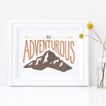 Load image into Gallery viewer, A white frame with a vase of yellow flowers next to the frame. The artwork in the frame has the words “Be adventurous” with arrows pointing to the word “be” and a brown mountain illustration underneath the word “adventure.”