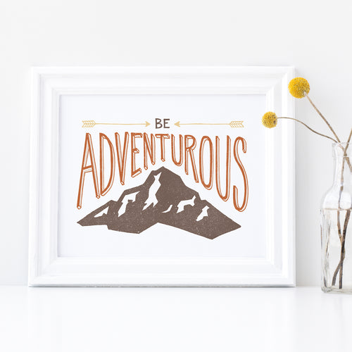A white frame with a vase of yellow flowers next to the frame. The artwork in the frame has the words “Be adventurous” with arrows pointing to the word “be” and a brown mountain illustration underneath the word “adventure.”